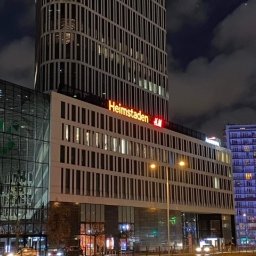 Pracownia Reklamy Plastica Tabernacka Sp. j - Nocny widok na budynek biurowy z neonowym napisem Heimstaden i logo H&M, otoczony innymi budynkami i rozświetlony ulicznymi lampami.