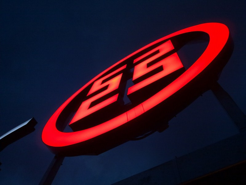 Podświetlany, czerwony znak firmowy na tle nocnego nieba, widoczny z dołu pod kątem.