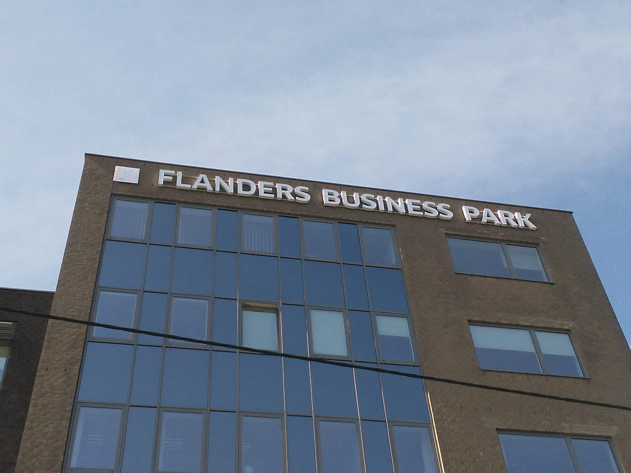 Budynek biurowy z cegły z dużymi oknami i napisem 'FLANDERS BUSINESS PARK' na górze