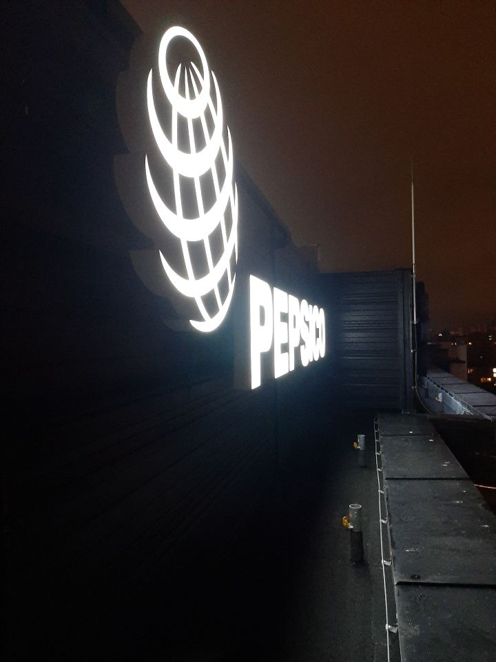 Podświetlane logo korporacyjne PepsiCo na budynku, widoczne z perspektywy dachu w nocy.