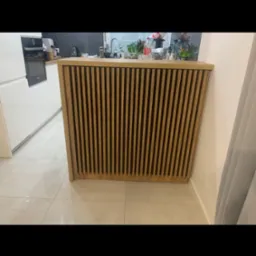 Blat kuchenny z drewnianymi lamelami w nowoczesnej kuchni, widok z boku, jasne płytki na podłodze, białe meble kuchenne w tle.