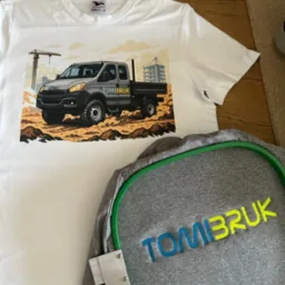 Biała koszulka z nadrukiem ciężarówki Iveco i szara bluza z haftowanym napisem 'TOMIBRUK' na drewnianym tle.