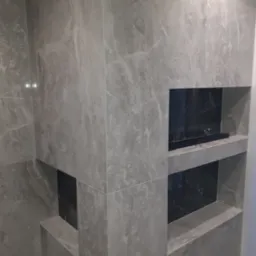 Szara marmurowa ściana z wnękami wyłożonymi czarnym marmurem, jedna z wnęk z półką, nowoczesna aranżacja łazienki.