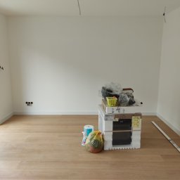Viacheslav Holovko - Pokój po remoncie z nową podłogą panelową, świeżo pomalowanymi ścianami, widoczne gniazdka elektryczne i listwy przypodłogowe, na środku pomieszczenia stos materiałów budowlanych i opakowań.