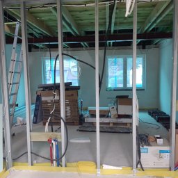 Viacheslav Holovko - Wnętrze w trakcie prac remontowych: widoczne metalowe profile konstrukcyjne, instalacje elektryczne i hydrauliczne, materiały budowlane w kartonach, surowy strop z drewnianych belek.