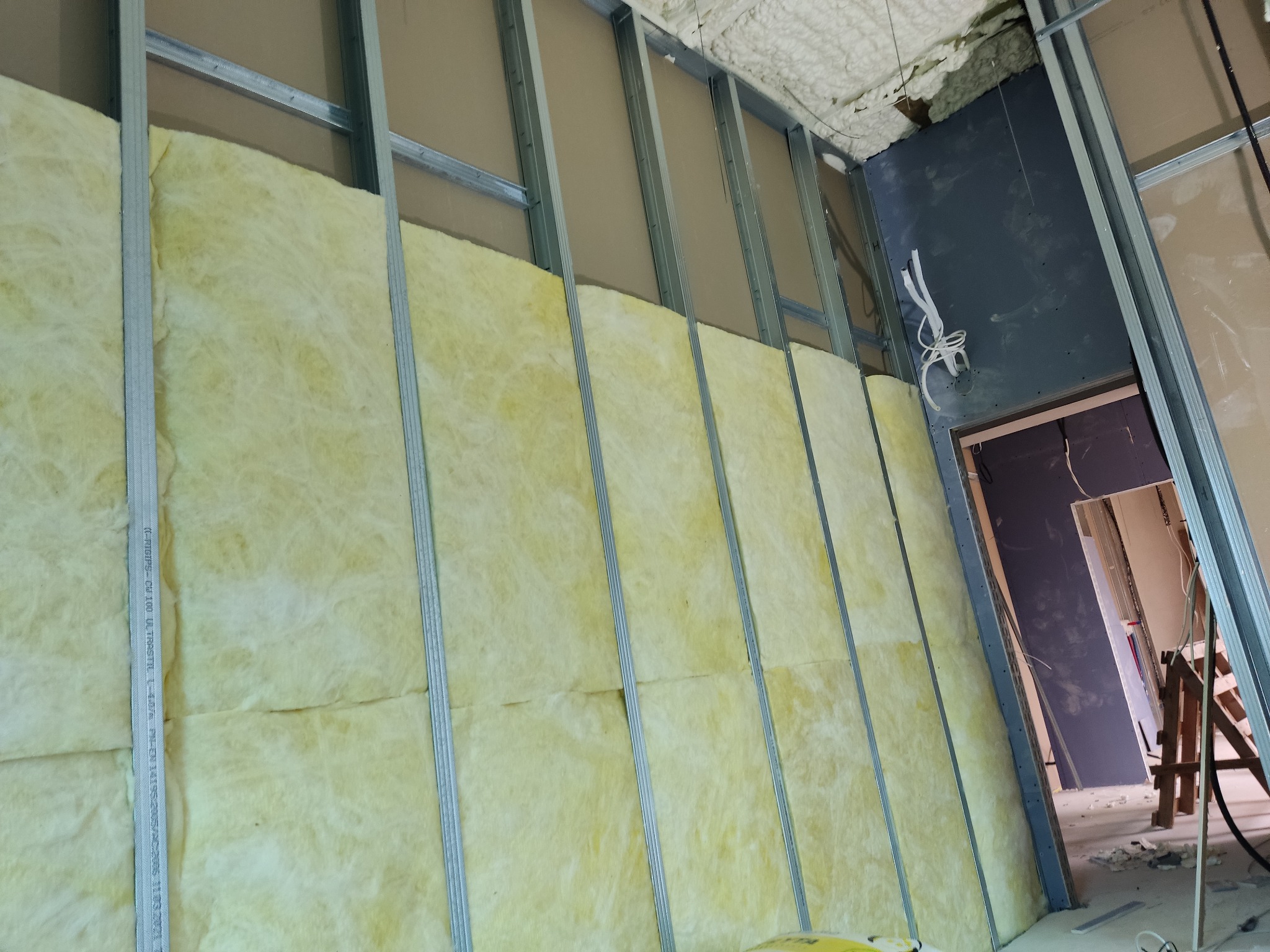 Montaż izolacji z wełny mineralnej w metalowym stelażu, widoczne fragmenty płyty kartonowo-gipsowej i instalacji elektrycznej.