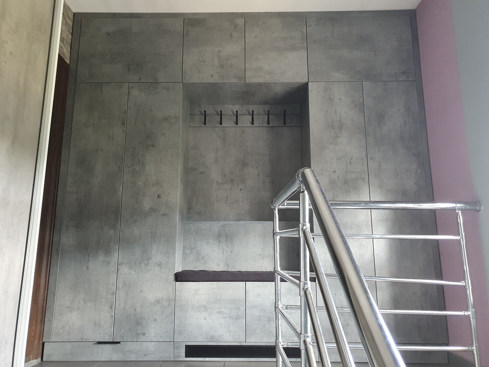 Szara szafa wnękowa z wnęką z siedziskiem i wieszakami, widok z góry ze schodów z metalową barierką.