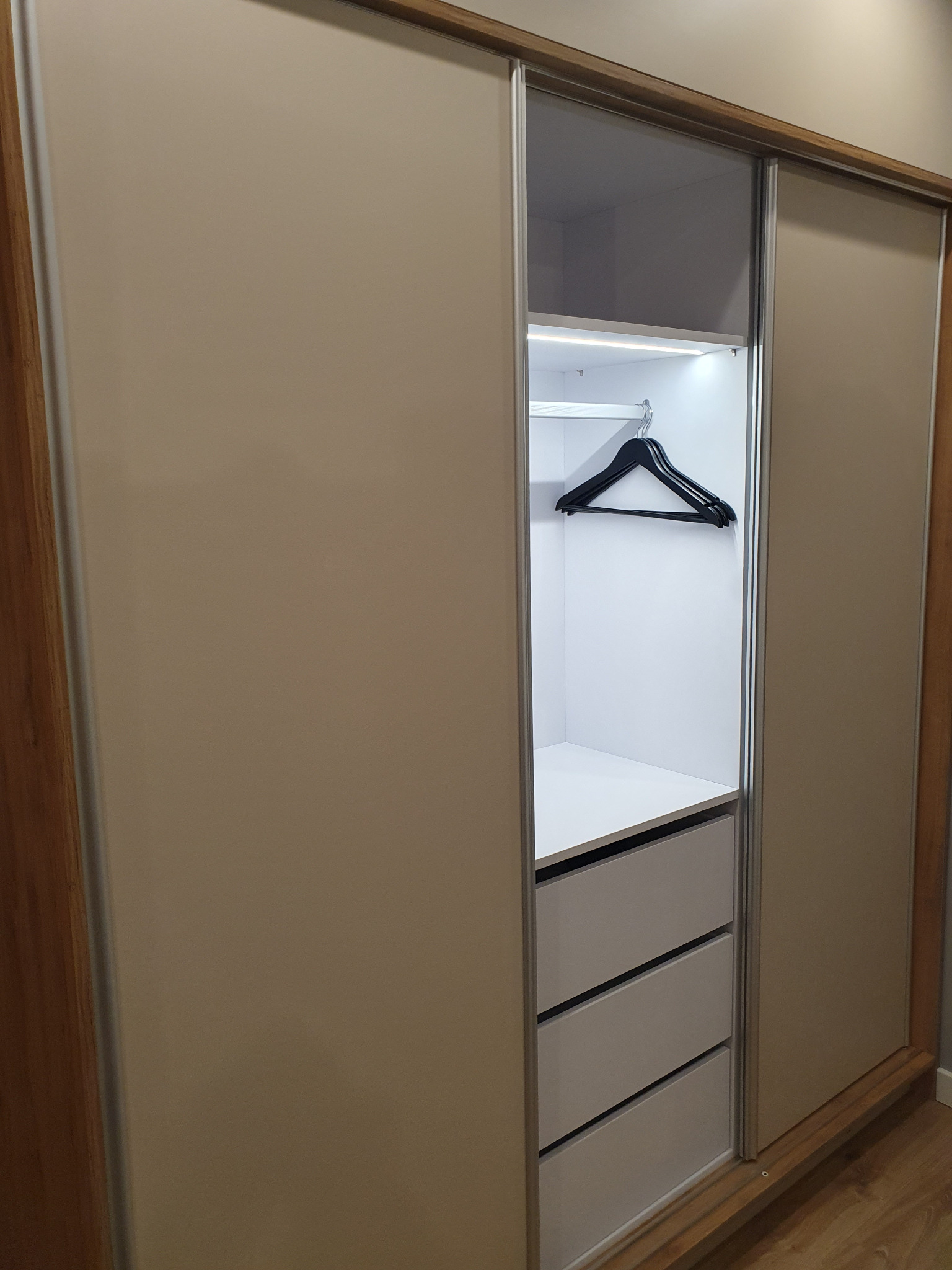 Szafa wnękowa z przesuwnymi drzwiami, oświetleniem LED i szufladami, widoczny wieszak. Realizacja z Wilkowic.