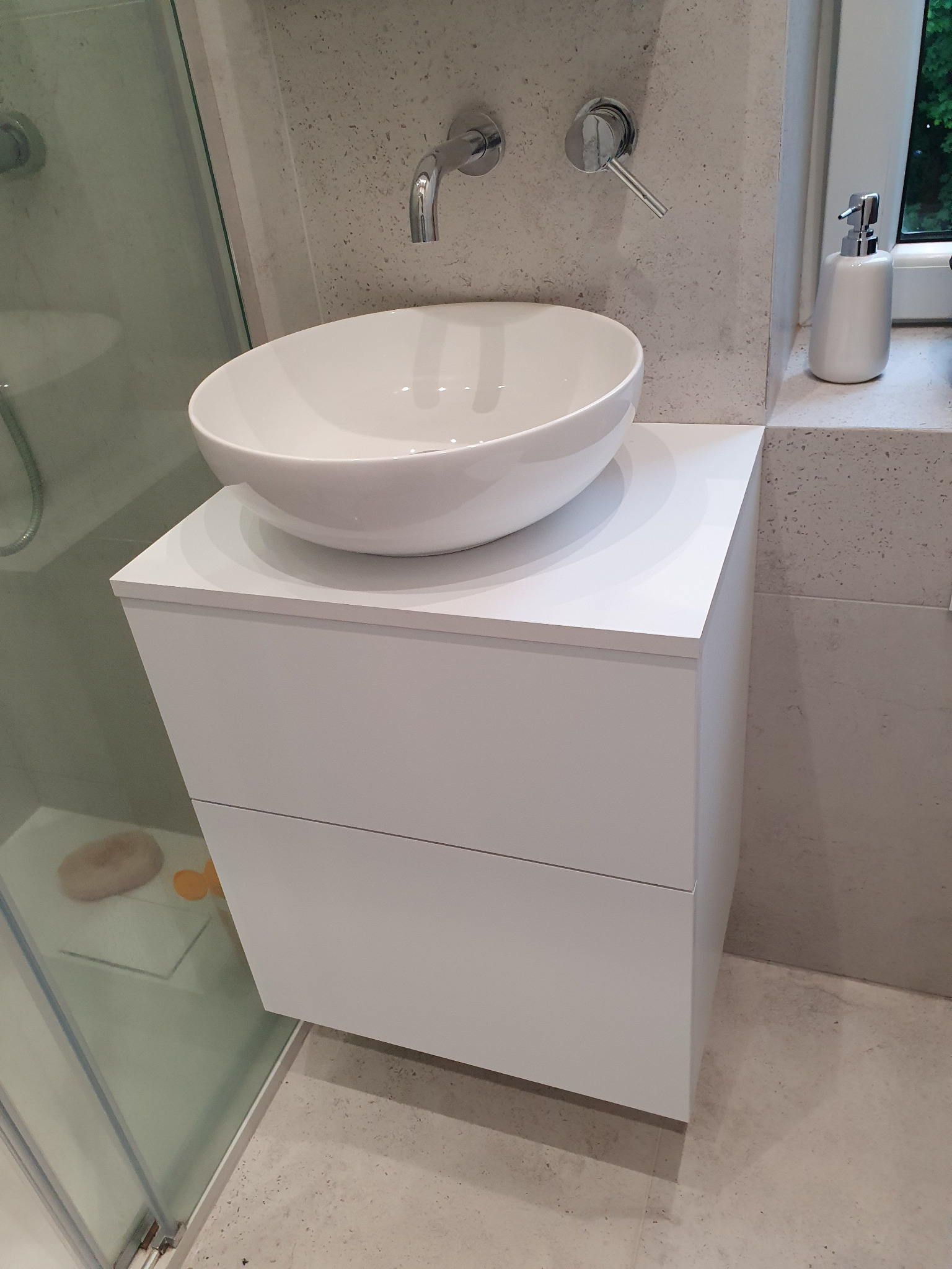 Biała szafka łazienkowa z umywalką nablatową w nowoczesnej łazience z kabiną prysznicową i armaturą w kolorze chromu. Minimalistyczny design.