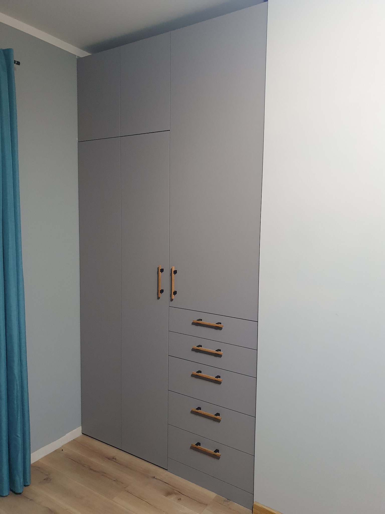 Szara szafa wnękowa z drewnianymi uchwytami, zintegrowana z szufladami, na tle jasnych ścian i podłogi. Minimalistyczny design.