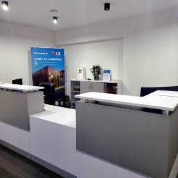 ODNAWIALNE ŹRÓDŁA ENERGII SPÓŁKA Z OGRANICZONĄ ODPOWIEDZIALNOŚCIĄ - Nowoczesne biuro z ladą recepcyjną i banerem reklamowym pompy ciepła monoblok LG Therma V. Minimalistyczny design, stonowana kolorystyka, oświetlenie punktowe.