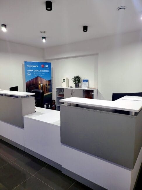 Nowoczesne biuro z ladą recepcyjną i banerem reklamowym pompy ciepła monoblok LG Therma V. Minimalistyczny design, stonowana kolorystyka, oświetlenie punktowe.