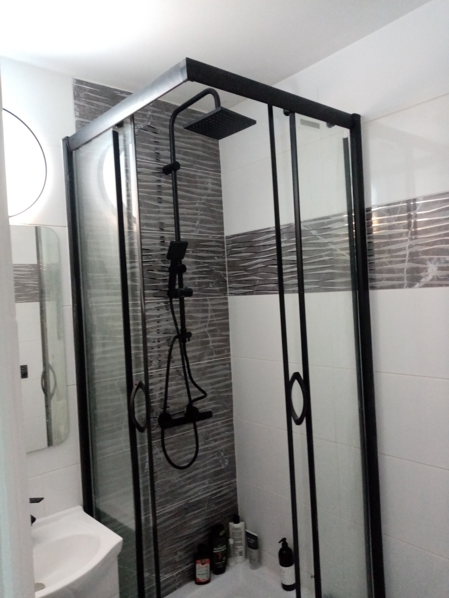 Kabina prysznicowa z czarnymi profilami i deszczownicą w łazience w Dąbrowie Górniczej, widoczna umywalka i fragment lustra.