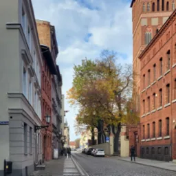 Ulica Piernikarska w Toruniu z budynkami biurowymi po obu stronach, w tle wieża kościoła i jesienne drzewa.