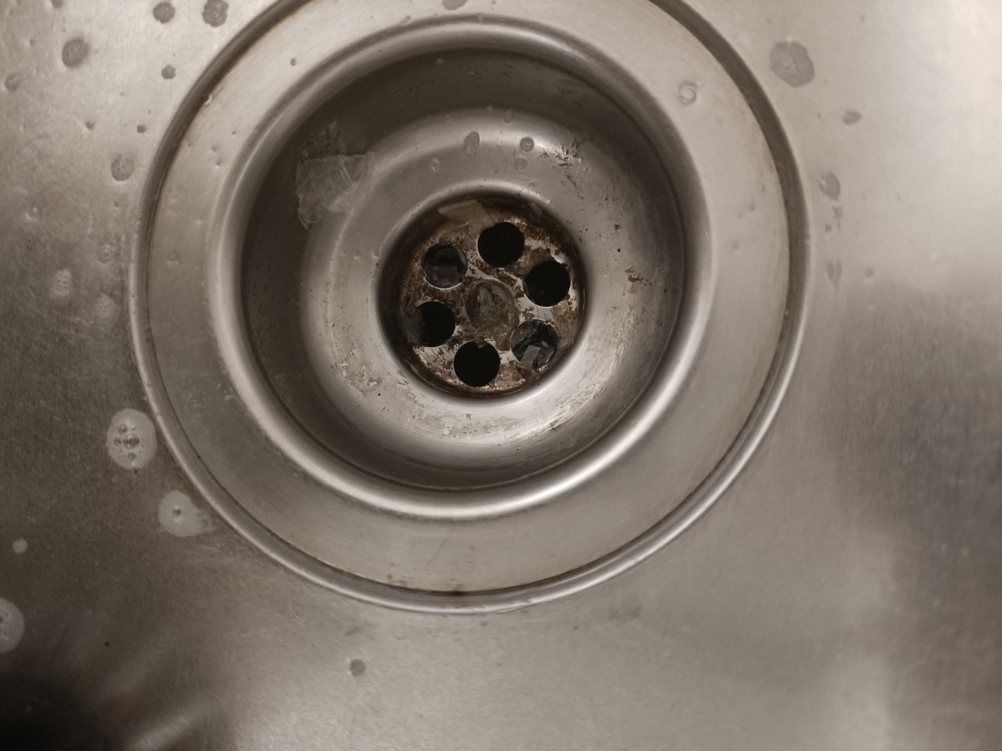 Metalowy odpływ zlewu z widocznymi resztkami jedzenia i śladami mydlin.
