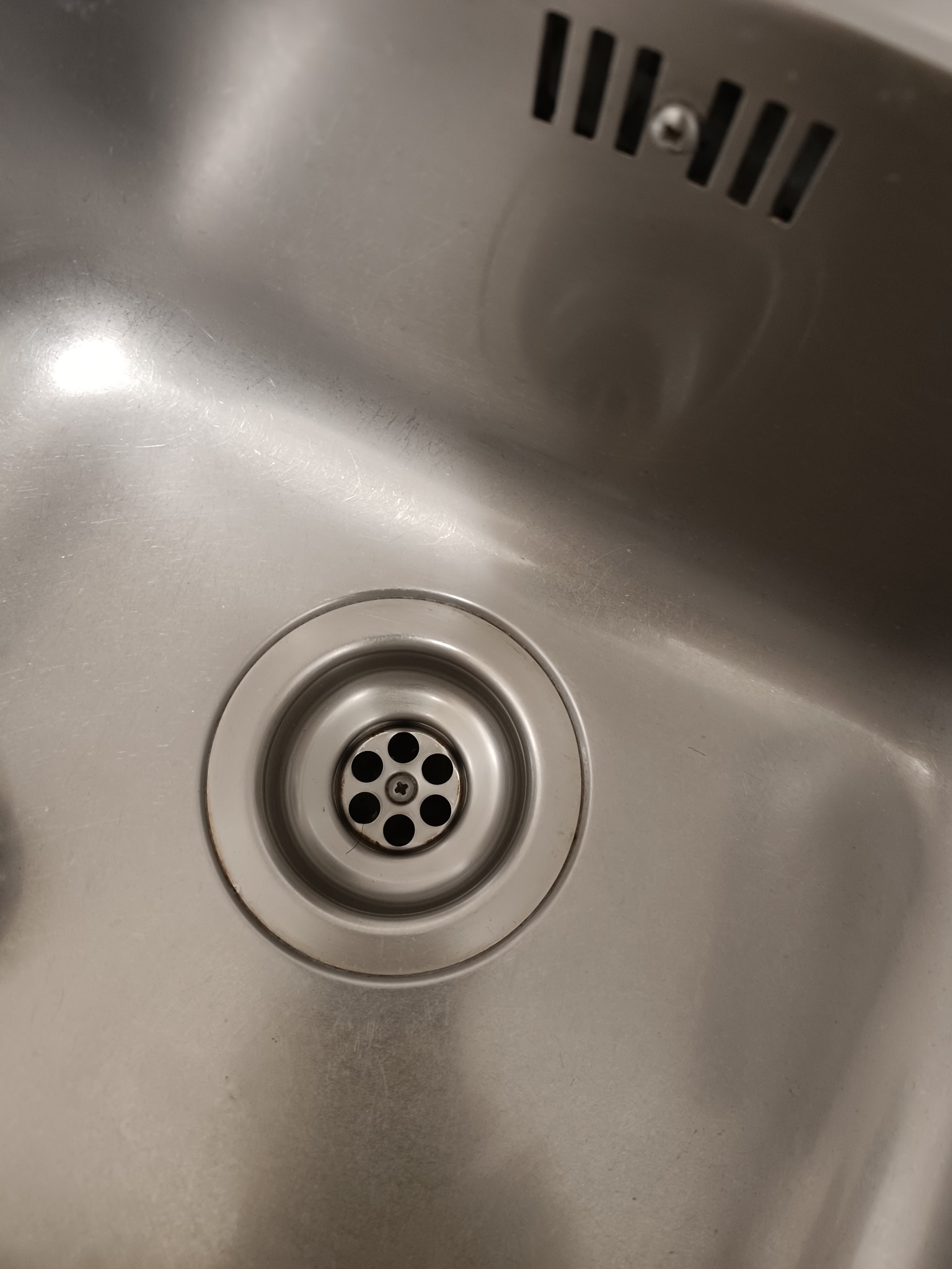 Metalowy zlew kuchenny ze stali nierdzewnej z widocznym odpływem i śladami użytkowania.