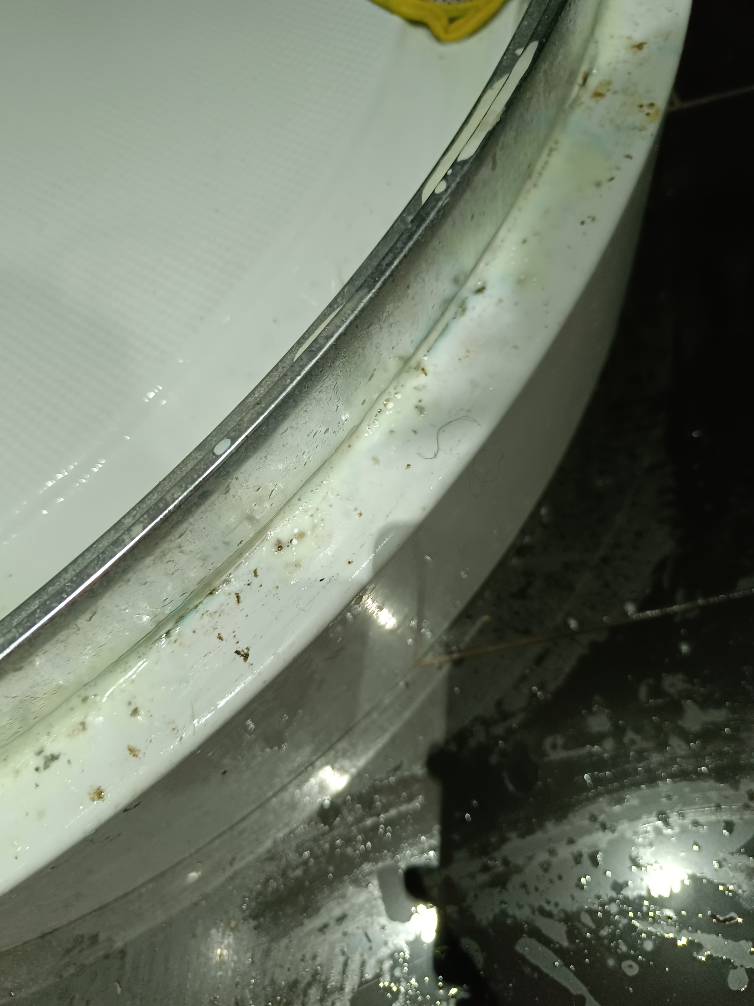 Brudna, biała wanna z osadami i włosami, widok z góry pod kątem, słabe oświetlenie.