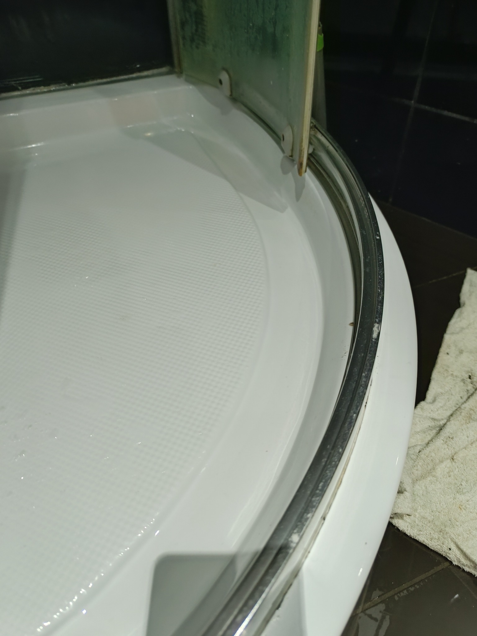 Brodzik kabiny prysznicowej z widocznymi śladami kamienia i zabrudzeń wzdłuż uszczelki, obok leży brudna ścierka.