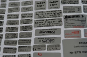 Arkusz z różnymi srebrnymi plombami gwarancyjnymi i informacyjnymi o różnych kształtach i rozmiarach, zawierający napisy takie jak 'PLOMBA GWARANCYJNA', 'Serwis: Firma MILAN', 'LinBOX', 'KOMSA'...