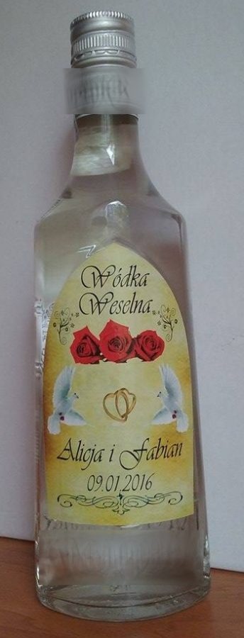 Szklana butelka wódki weselnej z spersonalizowaną etykietą z imionami Alicji i Fabiana oraz datą 09.01.2016, ozdobiona motywem gołębi, róż i obrączek.