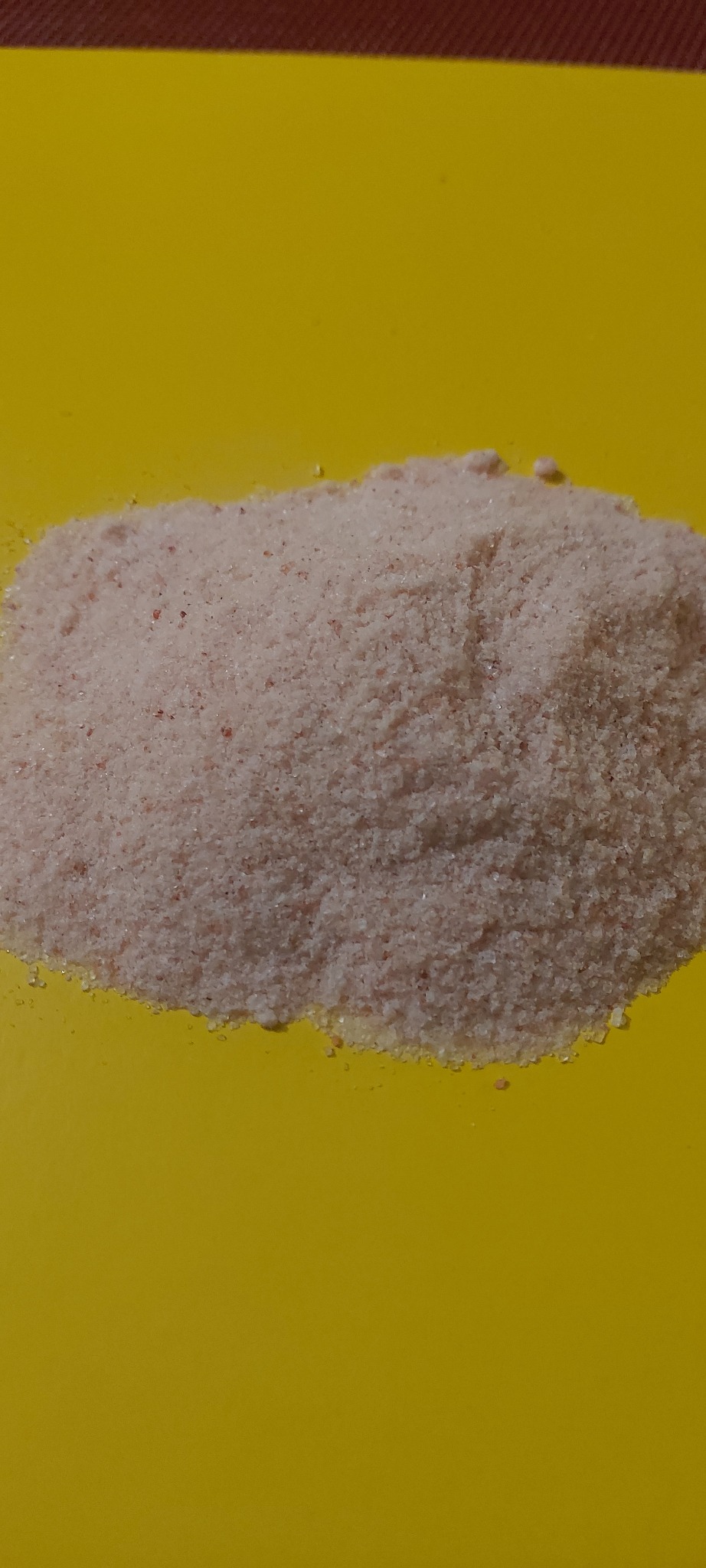 Niewielka pryzma jasnoróżowego granulatu na jaskrawożółtym tle, z widoczną drobną strukturą ziaren.