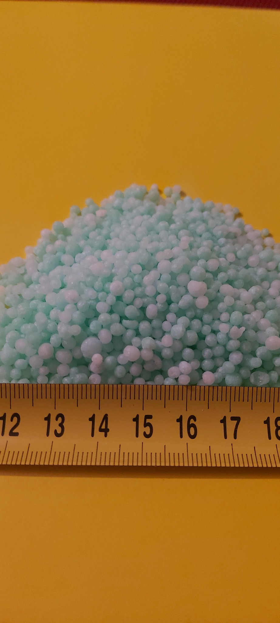 Kopuła jasnoniebieskich granulek na żółtym tle, z żółtą miarką mierzącą ich wysokość.