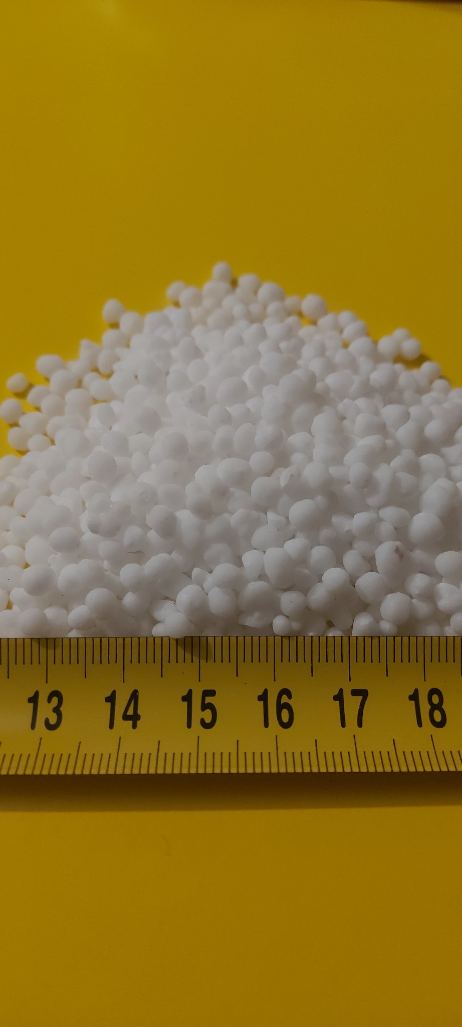 Kopuła białych granulek na żółtym tle, zmierzona żółtą miarką od 13 do 18 cm.