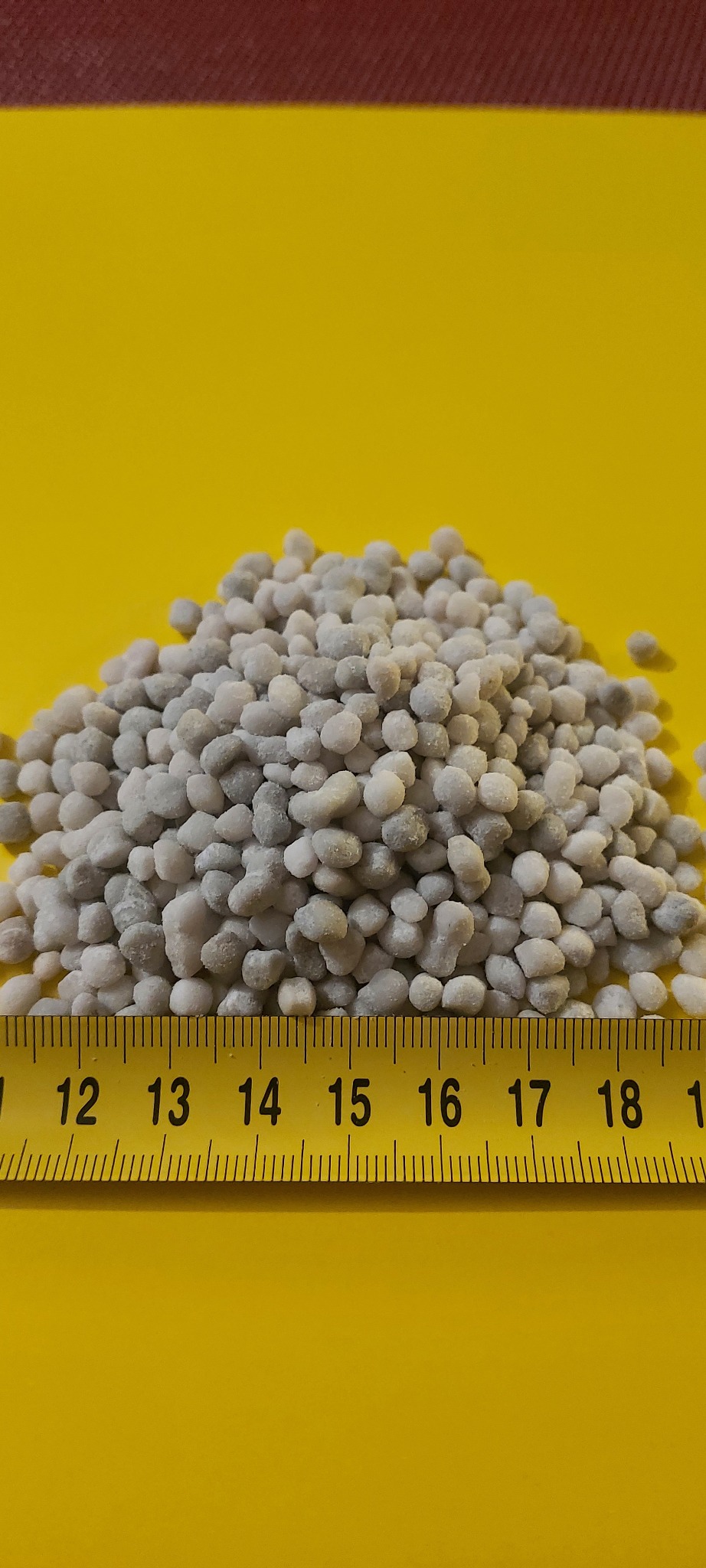 Górka szarego granulatu na żółtym tle, z linijką u dołu wskazującą wymiary.