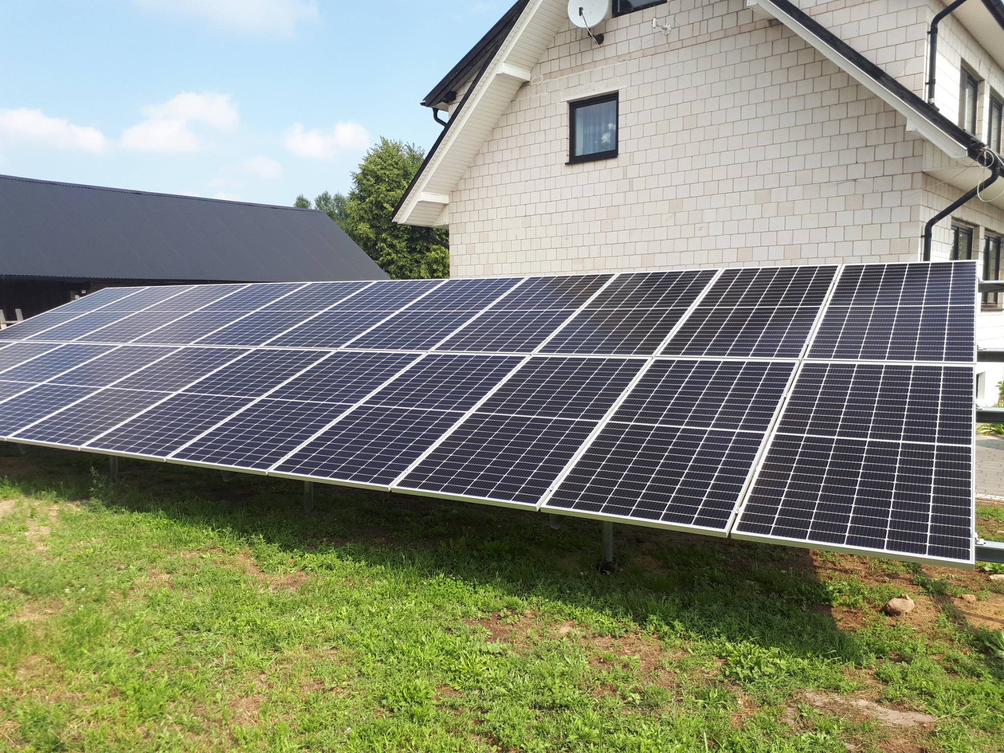 Panel słoneczny na trawniku przed domem z jasną elewacją, widoczne mocowania paneli.