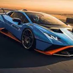 Błękitny samochód sportowy Lamborghini Huracan STO z pomarańczowymi akcentami, pędzący po torze wyścigowym podczas zachodu słońca, z widocznymi elementami zabezpieczeń toru po prawej stronie.