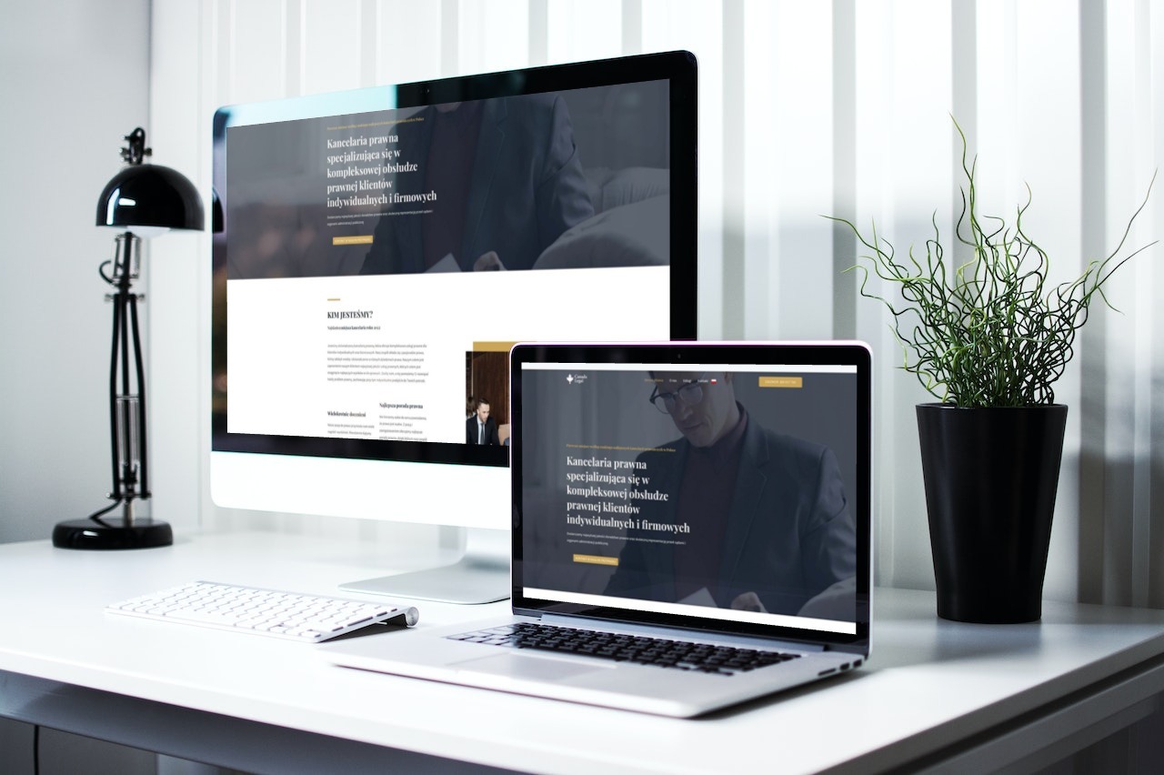 Prezentacja responsywnej strony internetowej kancelarii prawnej na monitorze i laptopie, minimalistyczne biurko z lampą i rośliną w tle.