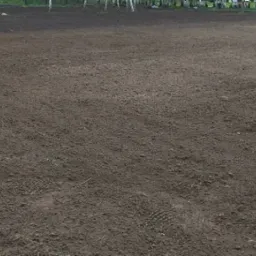 Równy, przygotowany teren pod przyszłą inwestycję, z widocznymi śladami opon i butów, otoczony drzewami.