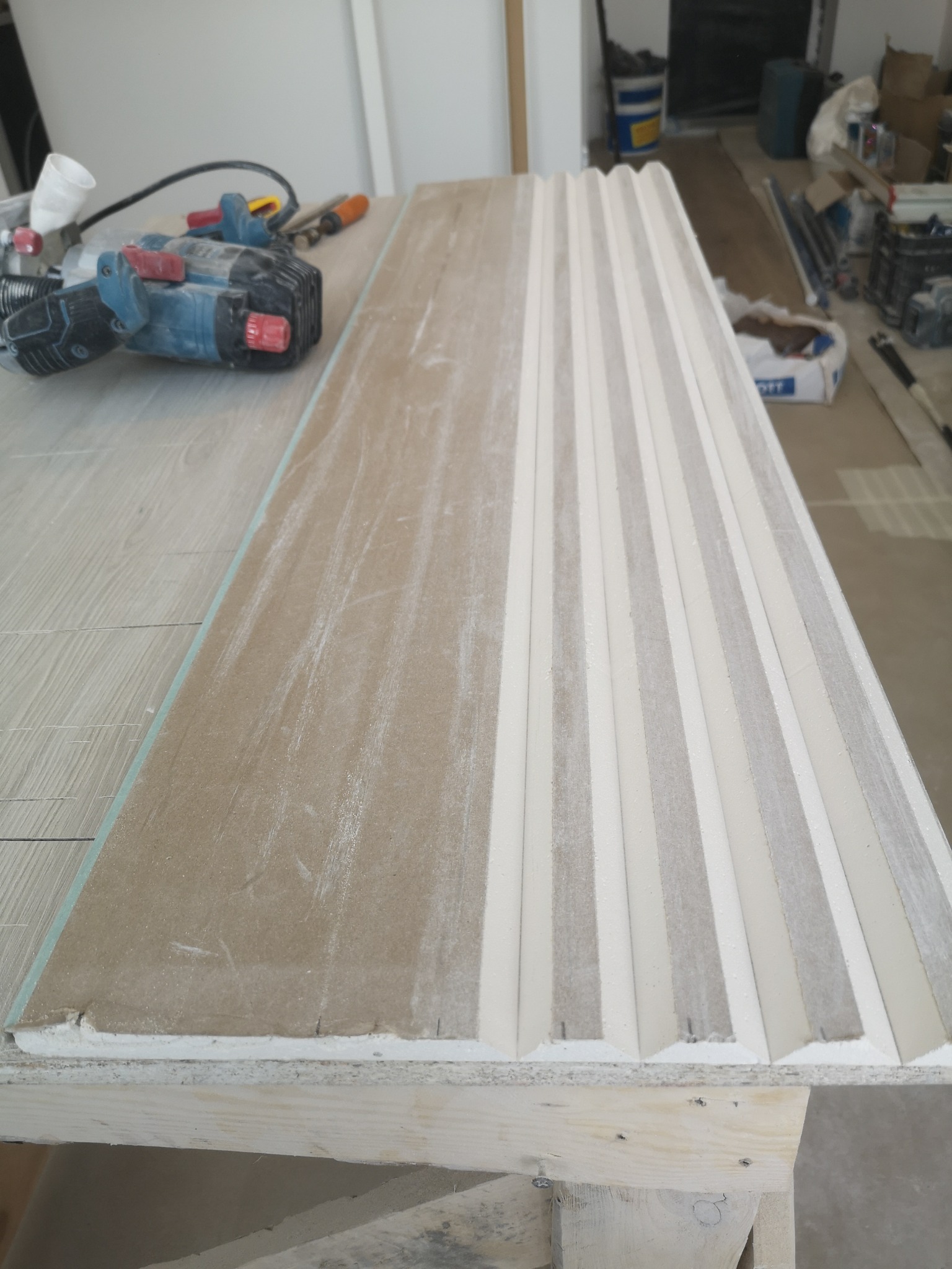 Przygotowanie płyty karton gips z frezowanymi rowkami i narzędziem do obróbki drewna na stole warsztatowym.