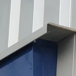 Detal zewnętrzny budynku przemysłowego z widocznymi śladami wilgoci po niedawnym myciu, krople wody na pomalowanej na niebiesko konstrukcji stalowej.