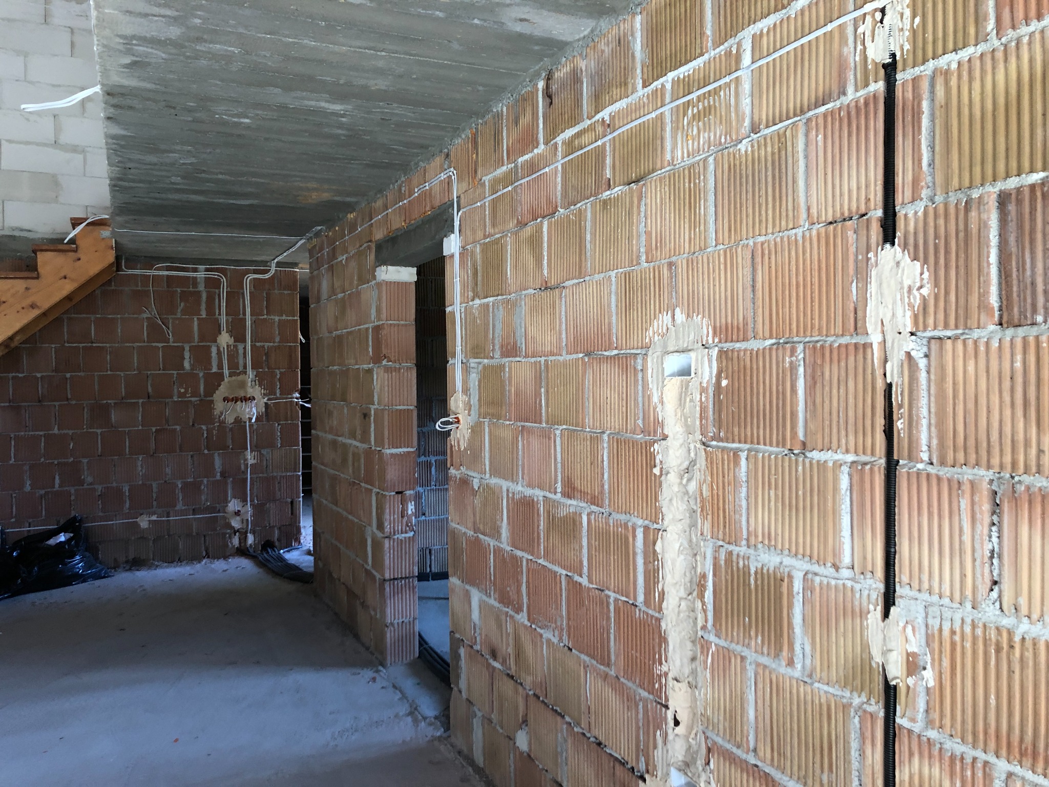 Wewnętrzne mury z pustaków ceramicznych z widocznymi, częściowo zamaskowanymi przewodami elektrycznymi w trakcie montażu.