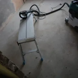Szlifierka do gipsu z odkurzaczem na aluminiowej drabinie w surowym wnętrzu. Przygotowanie do prac wykończeniowych.