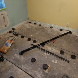 Iberhome - Przygotowanie podłoża pod wylewkę samopoziomującą: laser krzyżowy, poziomnice i regulowane podkładki dystansowe na surowym betonie w remontowanym pomieszczeniu.