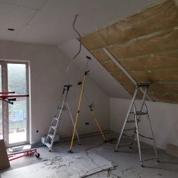 Iberhome - Poddasze w trakcie prac wykończeniowych: ocieplenie wełną, montaż płyt gipsowych. Widoczne drabiny, podnośnik do płyt i wystające przewody.