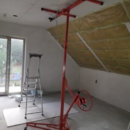 Iberhome - Montaż płyty G-K na poddaszu z użyciem podnośnika. Widoczna izolacja i drabina. Prace wykończeniowe w trakcie realizacji, surowe wnętrze.