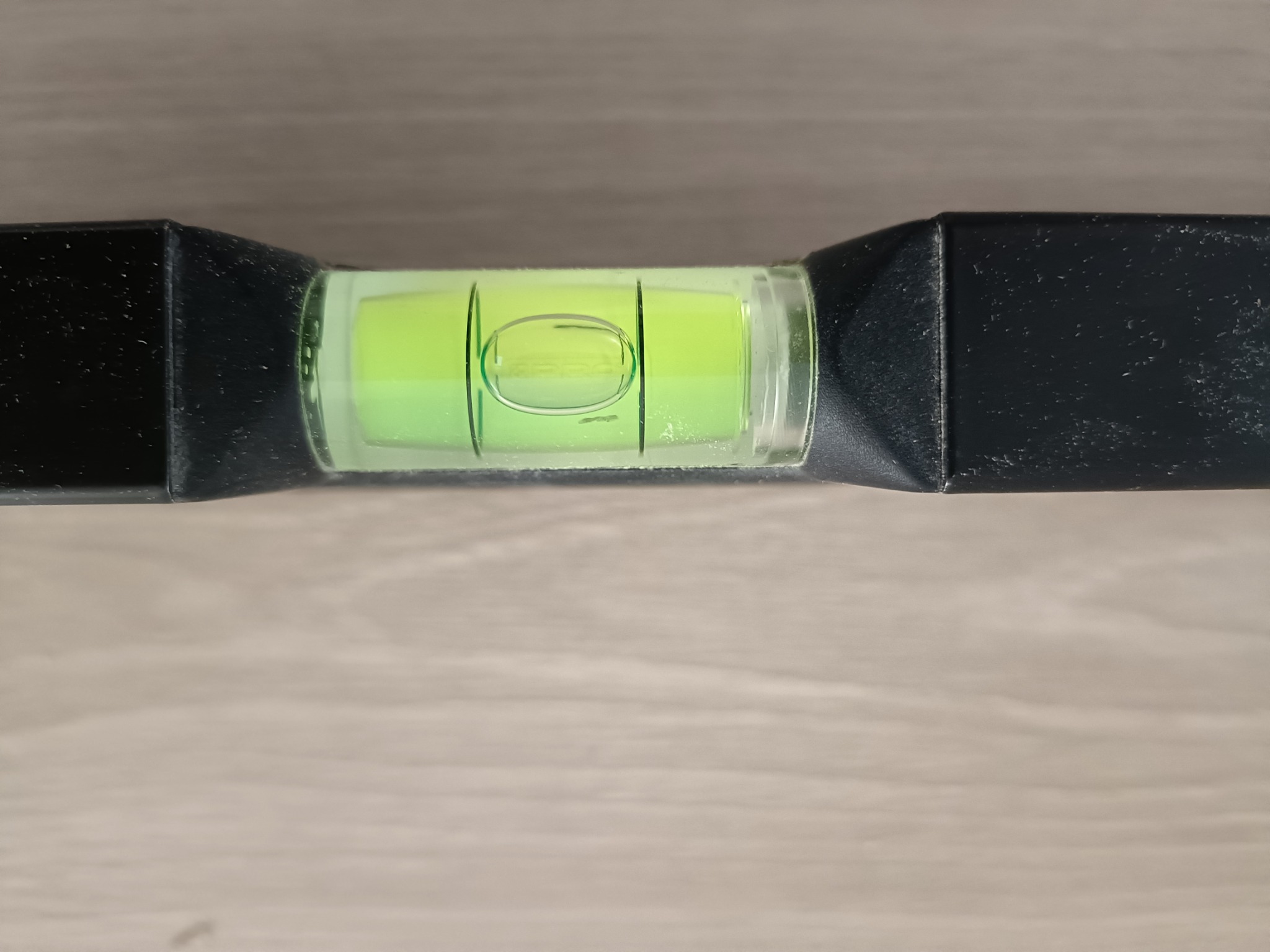 Poziomica w użyciu, bąbelek wskazuje idealny poziom na drewnianej powierzchni. Narzędzie precyzyjne, czarna obudowa, zielony płyn.