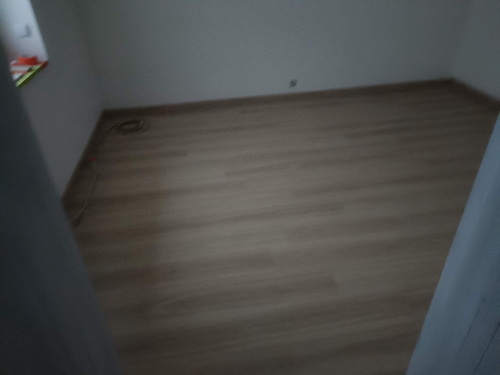 Pusty pokój z panelami podłogowymi w odcieniach brązu, świeżo po remoncie, widok zza futryny, ściany pomalowane na biało, widoczny fragment okna.