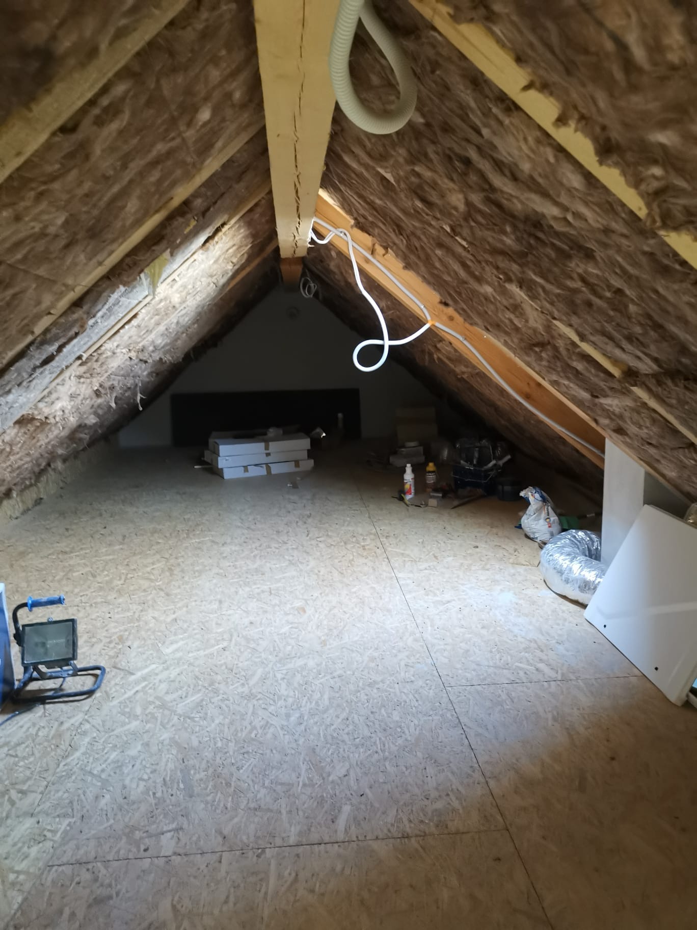 Ocieplone poddasze z widoczną izolacją z wełny mineralnej, drewnianą konstrukcją więźby dachowej, płytami OSB na podłodze i elementami instalacji.