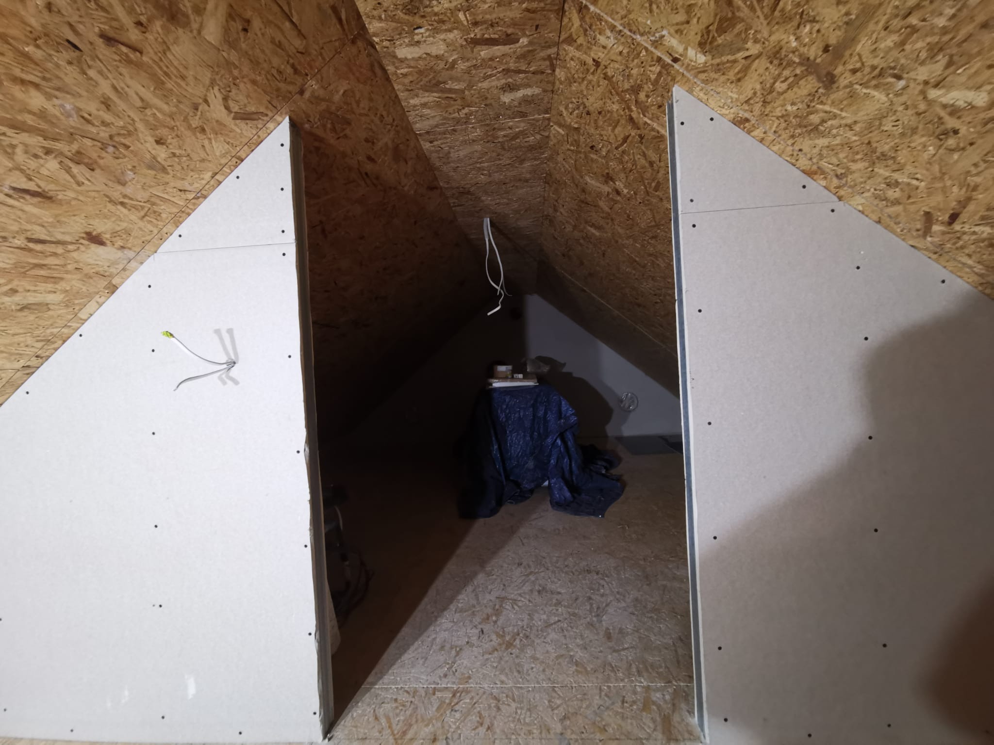 Płyty kartonowo-gipsowe zamontowane na poddaszu z widoczną konstrukcją drewnianą i przewodami elektrycznymi. Prace wykończeniowe w trakcie realizacji.