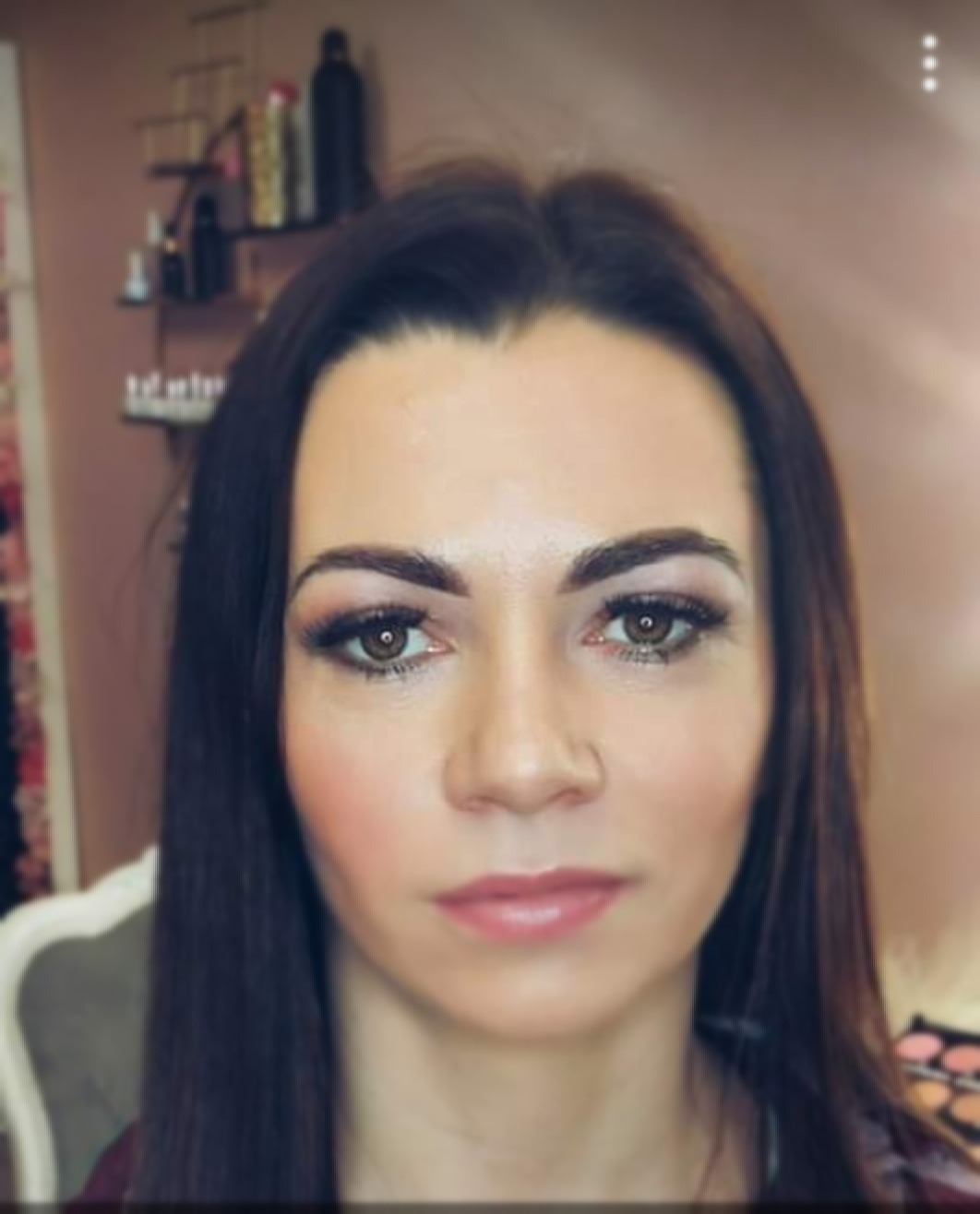 Portret kobiety z profesjonalnym makijażem, widoczne delikatne cienie do powiek i podkreślone brwi, w tle półka z kosmetykami.