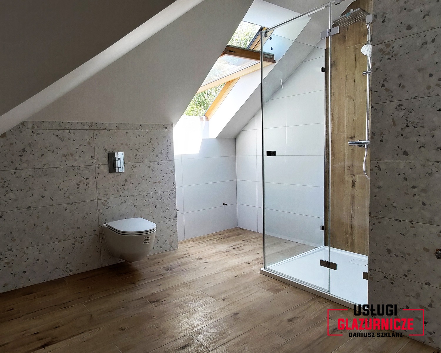 Wykończona łazienka na poddaszu ze skośnym oknem dachowym, płytki imitujące lastryko na ścianach, drewnopodobna podłoga, kabina prysznicowa ze szklanymi drzwiami i podwieszana toaleta.