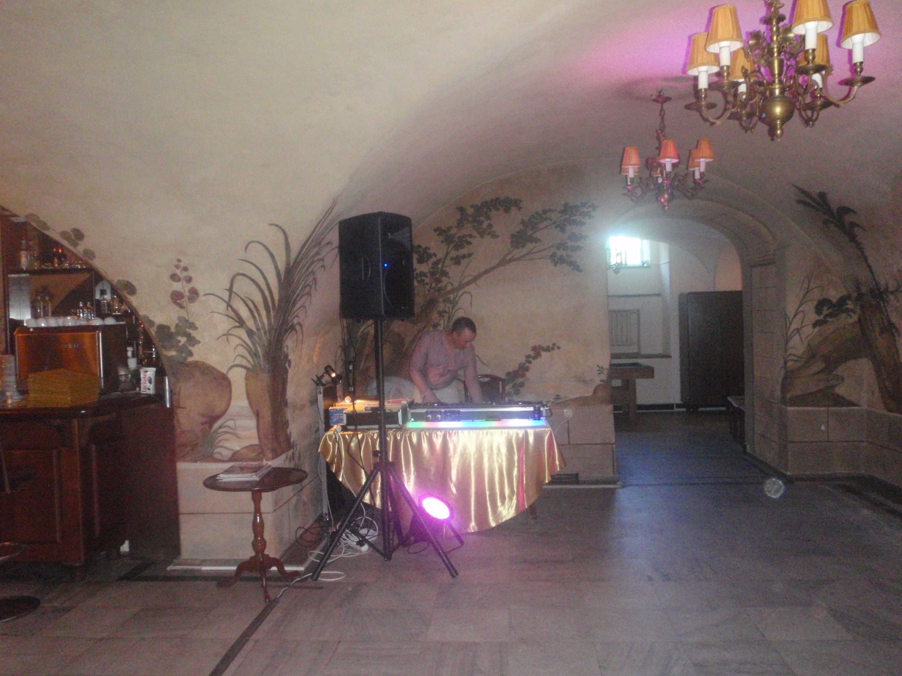 DJ obsługujący konsoletę na tle ściany z malowidłami w sali z barkiem i oświetleniem, przygotowany do występu.