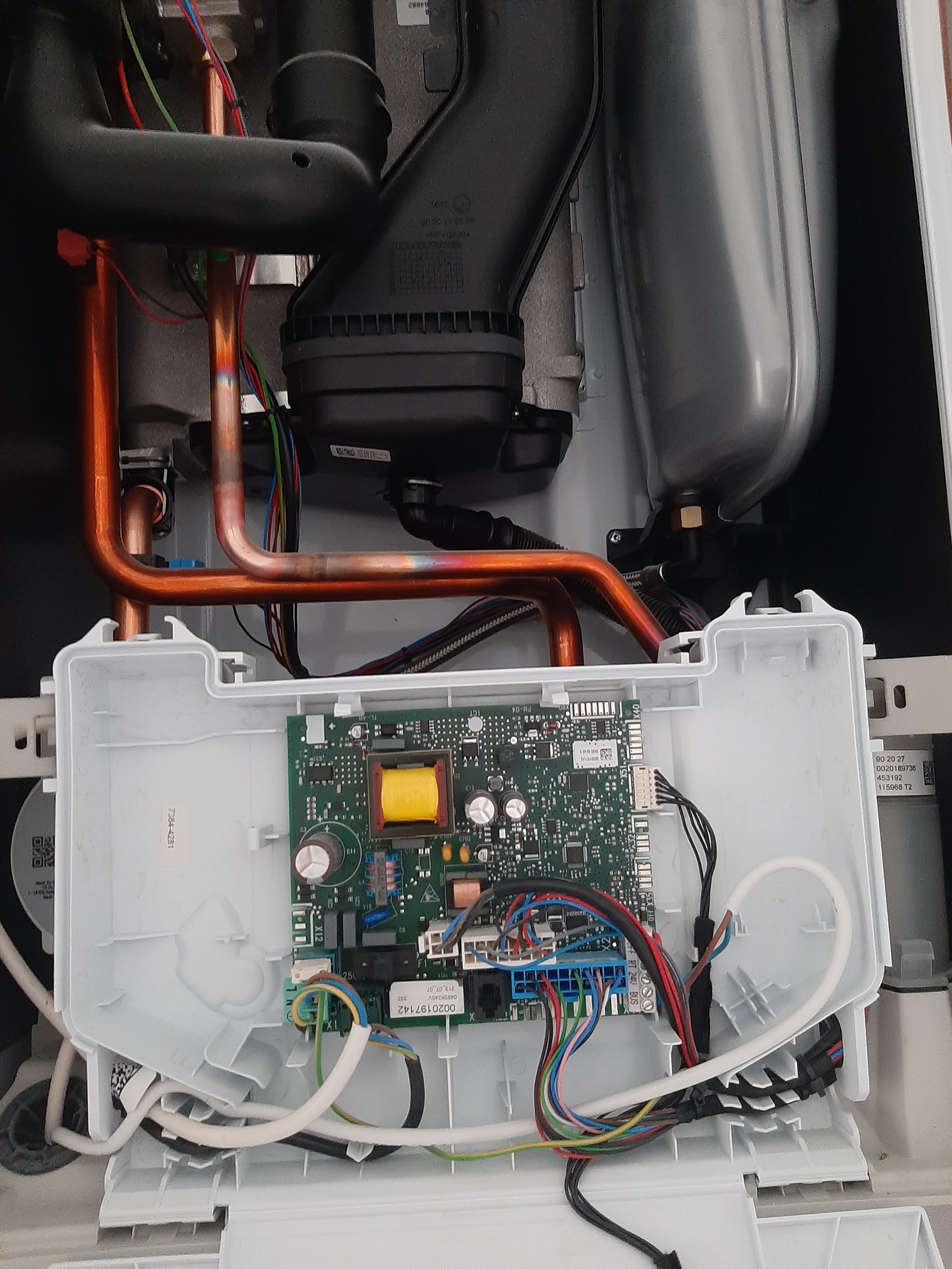 Wnętrze kotła gazowego z widoczną płytą sterującą, przewodami i miedzianymi rurkami, ukazujące skomplikowaną instalację i podłączenia elektryczne.