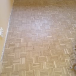 System Perfect Sp. z o.o. - Parkiet ułożony w kwadraty na podłodze w pokoju z żółtymi ścianami, widoczny fragment grzejnika i kawałek psiej łapy