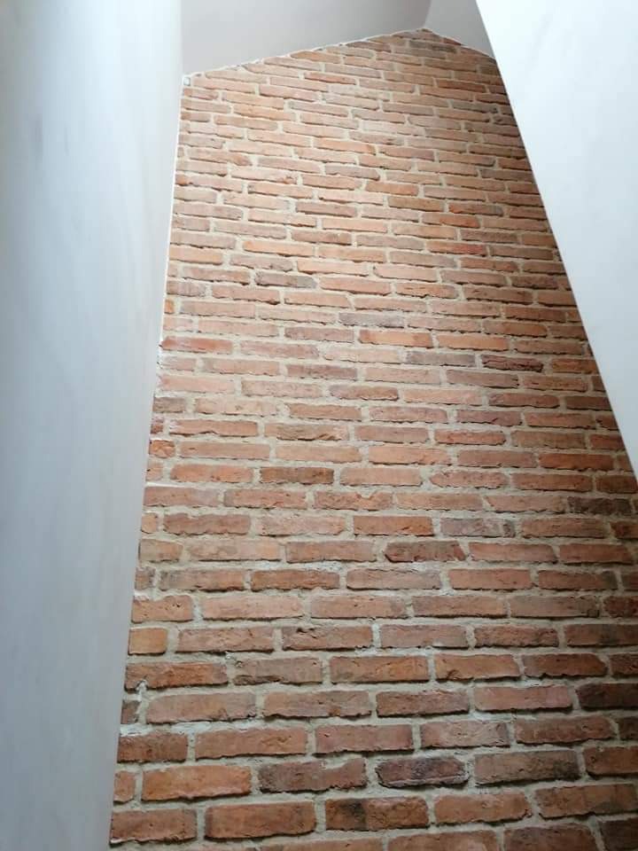 Wąska ściana wykończona czerwoną cegłą klinkierową, widziana pod kątem od dołu, z fragmentami gładkich, białych ścian po bokach.