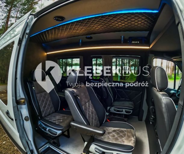Wnętrze luksusowo wyposażonego busa z oświetleniem LED, skórzanymi fotelami z pikowaniem i logo firmy na szybie.